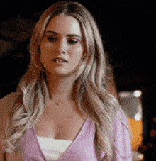 a woman with long blonde hair is wearing a purple sweater and a white tank top .