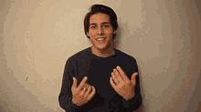 a young man in a black sweater is making a funny face with his hands in the air .