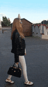 a woman in a black jacket and white pants is holding a black bag
