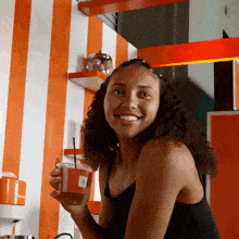a woman in a black tank top is smiling while holding a cup with a straw