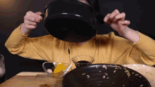 a person in a yellow sweater is holding a pot over their face