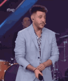 a man in a suit is standing in front of a microphone and a drum set .