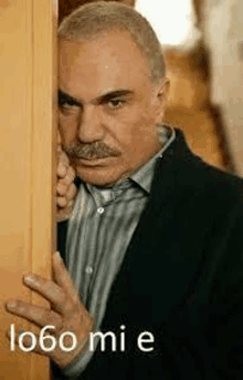 a man with a mustache is standing behind a door .