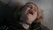 a woman wearing a choker and a black jacket is laying on the ground with her mouth open