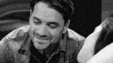 a man with a beard is smiling in a black and white photo while looking at a woman .