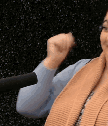 a woman wearing glasses and a sweater is giving a fist bump in front of a microphone
