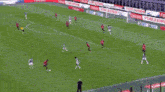 a group of soccer players are playing a game on a field with emirates in the background .