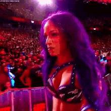 a woman with purple hair is standing in front of a crowd of people in a wrestling ring .