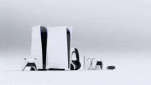 a playstation 5 is surrounded by controllers , headphones , and a charger .