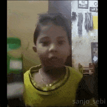 a little girl in a yellow shirt is making a funny face in a room .