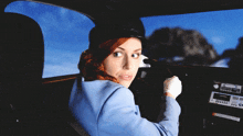 a woman in a blue suit is driving a car with a radio on the dashboard that says ' cbs ' on it
