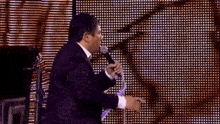 a man in a suit is singing into a microphone on stage