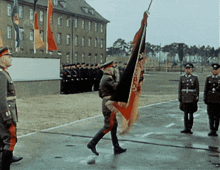 a man carrying a flag with the letter l on it stands in front of a group of soldiers
