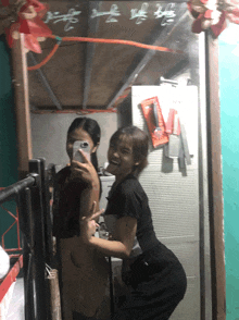two girls pose for a picture in front of a mirror with chinese writing on it