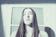a woman with long hair is standing in front of a window and looking up .