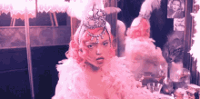 a woman with pink hair and feathers on her head looks at herself in a mirror