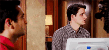 two men are looking at each other while sitting in front of a computer screen .