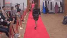 a woman in a pink dress is walking down a red carpet in front of a group of people .