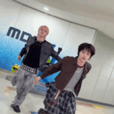 two young men are dancing in front of a wall that has the letter m on it