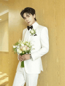 a man in a tuxedo holds a bouquet of flowers