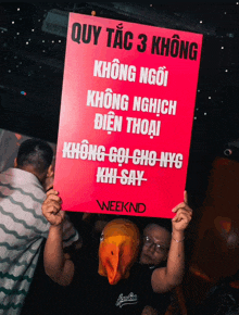 a man in a duck mask holds up a sign that says " weeknd "