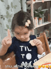 a little girl is sitting at a table eating a cracker and giving the middle finger ..