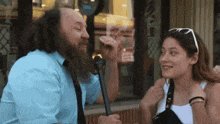 a man with a beard is talking to a woman with sunglasses on