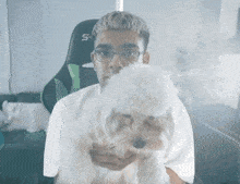 a man holding a small white dog with the letter s on his chair