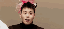a young man wearing a headband with cat ears and a pink bow on his head is waving his hand .