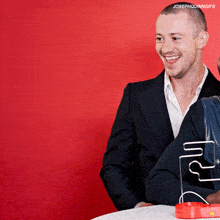 a man in a suit is smiling in front of a red background with the words josephquinngifs on the bottom