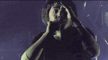 a man covering his face with his hands in a dark room with the letter d visible in the corner