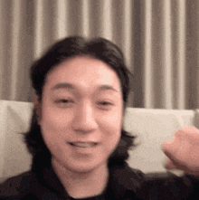 a man with long hair is sitting on a couch and making a face .