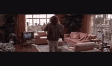 a woman is standing in a living room with a couch , chair , and television .