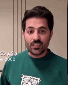 a man with a beard wearing a green sweatshirt is making a funny face .
