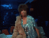 a woman in a fur coat is smoking a cigarette in a dark room