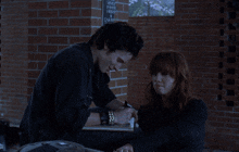 a man and a woman are sitting in front of a brick wall with a sign that says ' smoke ' on it