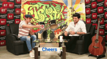 two men are sitting in front of a table that says cheers on it