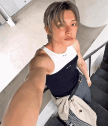 a man in a black tank top is taking a selfie while standing on stairs .