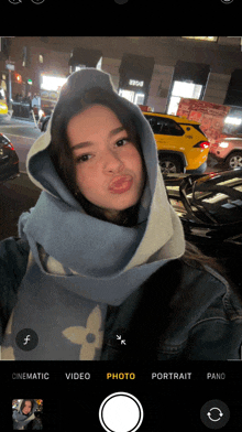 a woman wearing a scarf and a hoodie is taking a selfie with a camera