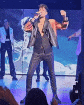 a man in a leather jacket sings into a microphone on a stage
