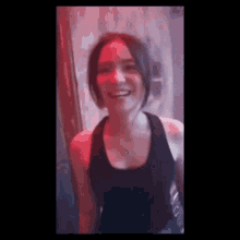 a woman in a black tank top is smiling and laughing in a dark room .