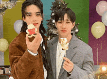 a couple of men are standing next to each other holding a cookie on a stick .
