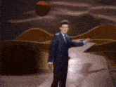 a man in a suit and tie is standing on a stage in front of a desert landscape .