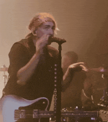 a man singing into a microphone with a guitar in front of him