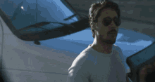 a man wearing sunglasses stands in front of a car