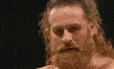 a man with a beard and long hair is standing in a boxing ring .