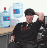 a man wearing a shirt that says hi is sitting in front of a water cooler