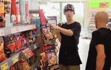 a man wearing a hat that says old is standing in front of a shelf full of chips