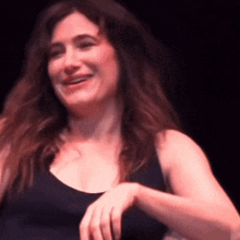 a woman in a black tank top is smiling with her hands on her hips