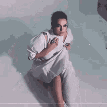 a woman in a white dress is sitting on a bed holding a white bag .